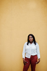 Formally dressed african american business woman in white blouse and red trousers isolated on yellow background. Successful dark skinned businesswoman.