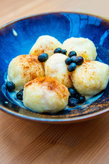 Six homemade sweet dumplings served with vanilla cream and blueberries in blue ceramic vintage bowl