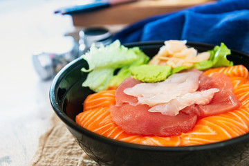 Japanese Chirashi made with assortment of three raw fishes, salmon, tuna and cod fish served on white vinegary rice with Wasabi sauce and ginger slices on top in a bowl.