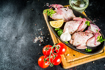 Cooking healthy diet lunch concept. Three whole quails with spices, herbs, vegetables, olive oil, for cooking on a black stone concrete table copy space