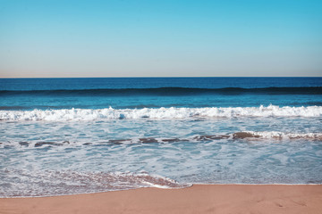Empty ocean beach with small waves and foam.