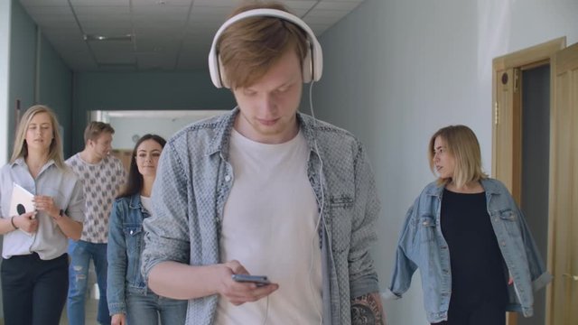 A young man in headphones walks along the inversion corridor, listens to music and does not pay attention to people. It is in its own world. An introvert walks through the college hall