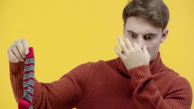 man in sweater smelling stinky sock isolated on yellow
