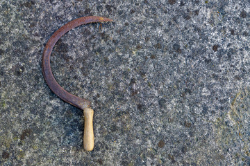 Detail of an old concrete wall covered with lichens, with an old and rusty sickle. Background. Vintage