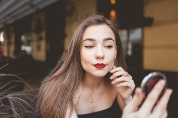 Portrait of a beautiful girl with a mirror in her hands sitting at a cafe table