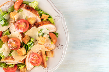 A close-up of a chicken Caesar salad, shot from above on a light blue background with a place for text
