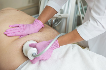 Closeup photo of fat man with big belly having cavitation procedure removing cellulite on abdomen in modern beauty clinic