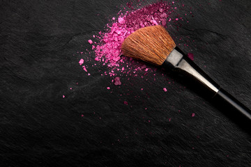 Make-up brush with vibrant crushed cosmetics, shot from the top on a black background with a place for text, a beauty design template for a makeup artist's business card