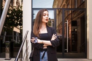 Stylish business lady in jacket with glasses in hands on background of office building