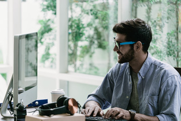 caucasian working man with beard and mustache in casual shirt using desktop computer