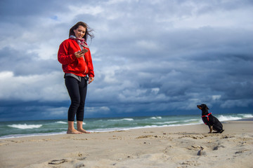 Młoda dziewczyna bawi się z pieskiem pinczerem miniaturowym ratler na plaży nad morzem