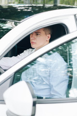 Young serious man looking ahead while sitting behind the wheel of his white car