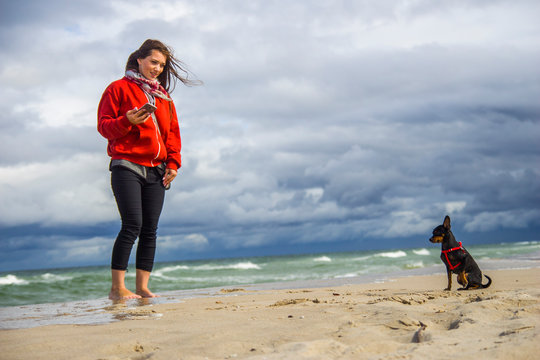 Młoda dziewczyna bawi się z pieskiem pinczerem miniaturowym ratler na plaży nad morzem