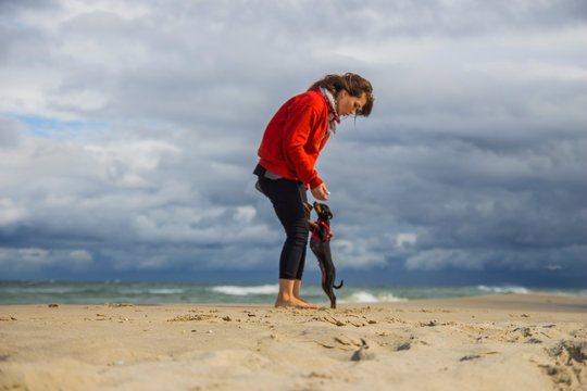 Młoda dziewczyna bawi się z pieskiem pinczerem miniaturowym ratler na plaży nad morzem