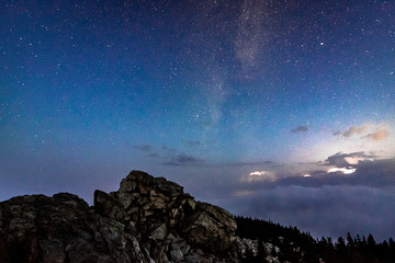 Milky Way galaxy in the night sky above rocky mountain and stormy clouds