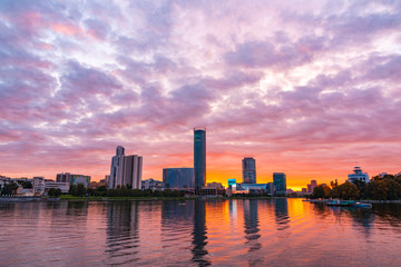 Beautiful purple and orange cloudy sunset at the city pond. Cityscape of Yekaterinburg, Russia with skyscrappers reflecting in water