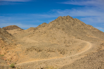 desert sand stone wilderness dunes dry scenery landscape wasteland environment with ground trail bare mountain peak and vivid blue sky 