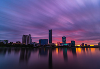Beautiful purple and orange cloudy sunset at the city pond. Long Exposure cityscape of Yekaterinburg, Russia with skyscrappers reflecting in water