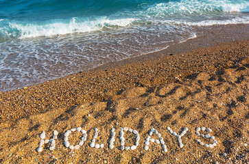 Holidays sign on the beach made from small rocks. Vacations concept