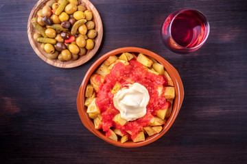 Patatas bravas, Spanish potatoes, with a glass of wine and olives, shot from the top on a dark background with a place for text