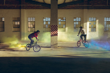BMX riders in an empty warehouse using smoke grenades