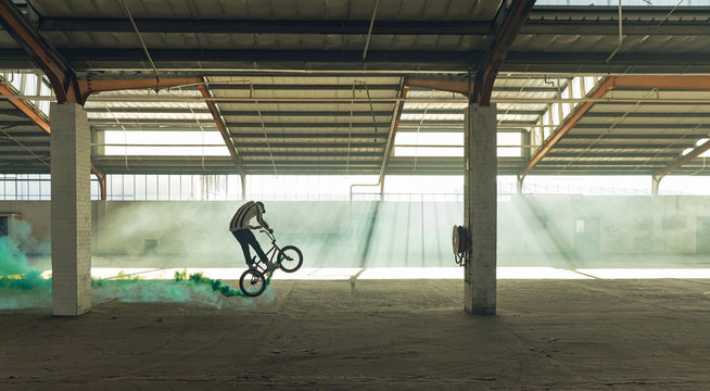 BMX rider in an empty warehouse using smoke grenade