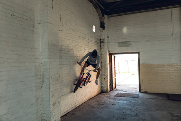 BMX rider riding on the wall in an empty warehouse