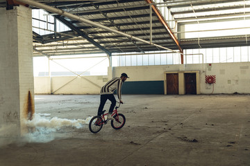 BMX rider in an empty warehouse using smoke grenade
