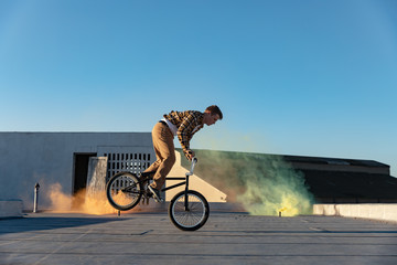BMX rider on a rooftop using smoke grenades
