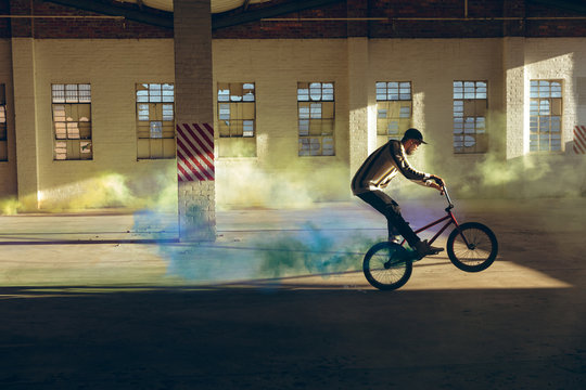 BMX rider in an empty warehouse using smoke grenade - Powered by Adobe