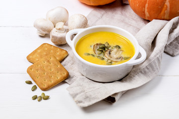 Bowl of Tasty Homemade Pumpkin Cream Soup decotated with Mushrooms and Pumpkin Seeds White Wooden Background View from Above Galette Horizontal