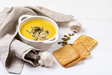 Bowl of Tasty Homemade Pumpkin Cream Soup decotated with Mushrooms and Pumpkin Seeds White Wooden Background View from Above Galette Horizontal