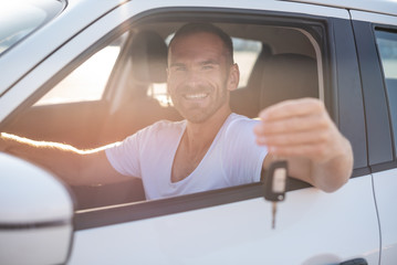 A man in a white car shows a key. Buying or renting a car - concept.
