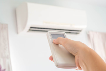 Hand using remote control directed on air condition in  white room