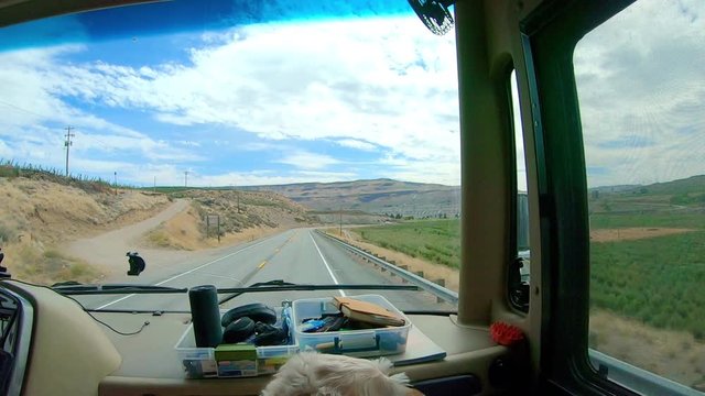 POV of the passenger in a large class A Recreational Vehicle while driving through the Okanogan Highlands of north central Washington State with a labradoodle dog in the foreground