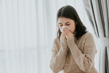 Sick Asian woman using a tissue to sneeze at home