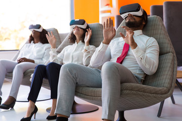 Amazed business colleagues relaxing in office rest room. Man and women wearing virtual reality...