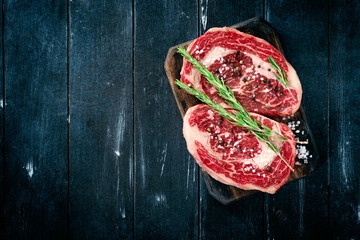 Two fresh beef steaks on a wooden Board with salt and pepper on a dark background. The concept raw...