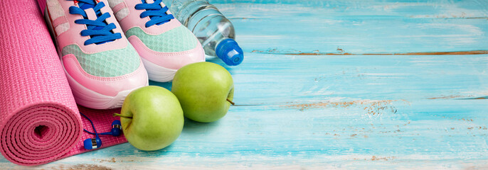 Pink yoga mat, sport shoes, bottle of water and apples on blue wooden background. Sport, healthy...