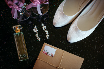 Beautiful set of wedding accessories bride. Morning bride's. White shoes, pearl earrings, and perfume on a shiny black surface.