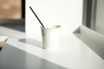 One simple takeaway paper cups on a white wooden table with a black paper tube