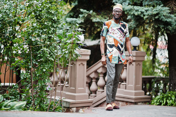 Obraz premium Handsome afro american man wearing traditional clothes, cap and eyeglasses in modern city.