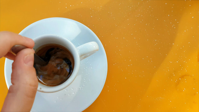 Top view of hand stirring sugar in coffee