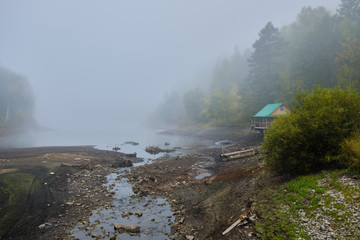 House hunting on the shore of the lake at dawn in the fog. Log home, lake mist
