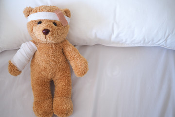 Teddy bear lying sick in bed With a headband and a cloth covered