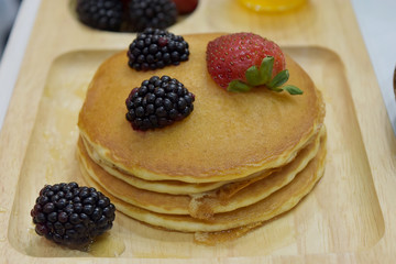 Fresh made delicious pancakes with berries, black berries honey and maple syrup on wooden plate. Healthy  breakfast concept.