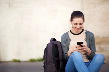 smiling female student sitting on floor outside and looking at mobile phone