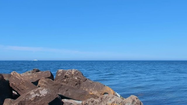 Scenic seascape with huge cobblestones and white yaght on sea in wild nature. at sunny day. Blue clear water surface with ripple and sky on nature seascape. Tourism, travel and vacation concept.