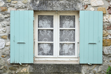 Fenêtre avec des volets vert. La façade est en pierre 