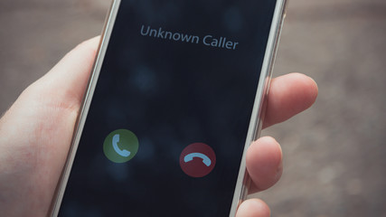 Unknown caller. A woman holds a phone in his hand outdoors in a park and thinks to end the call. Incoming from an unknown number. Incognito or anonymous